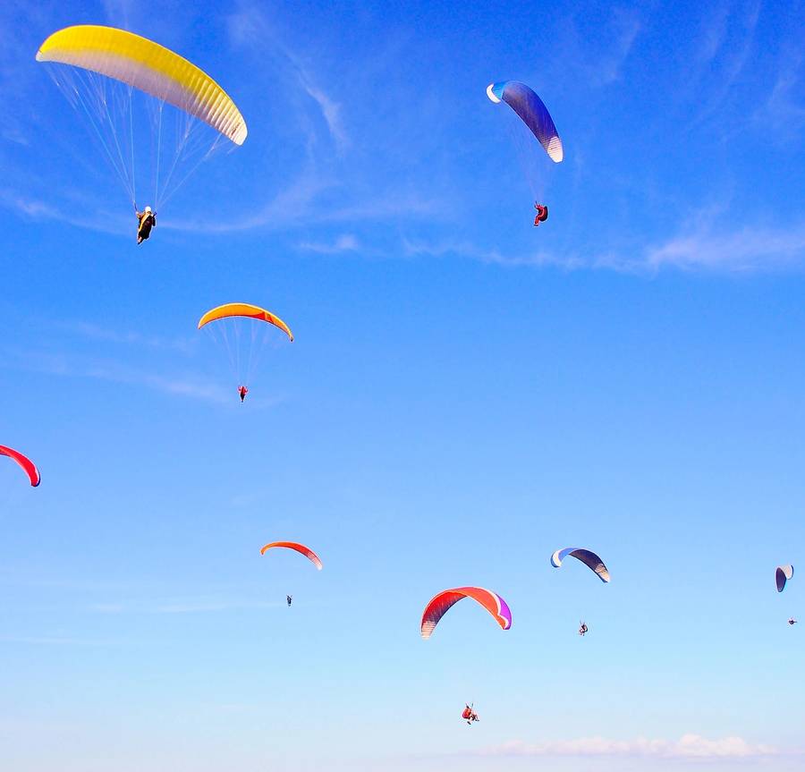 Different colored paragliders spin against the blue sky